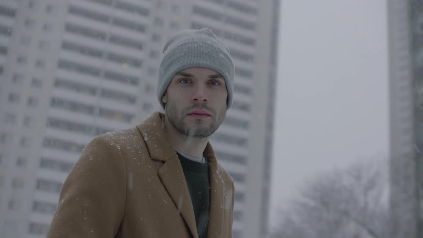 A man stands outside while it snows and looks around