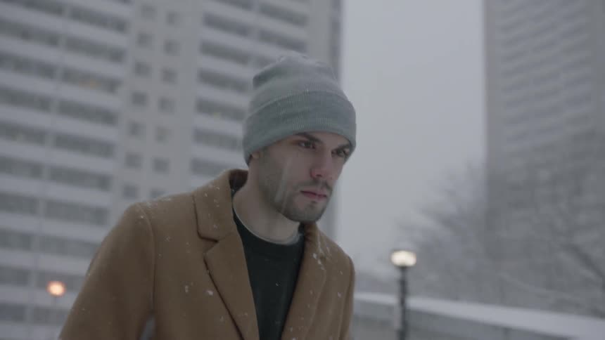 A man is walking in the city while it snows