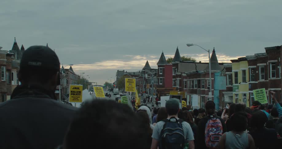 Crowd of people standing in town on a cloudy day some holding signs