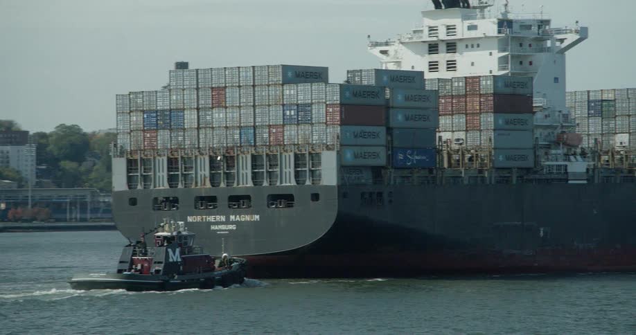 A tugboat is guiding a shipping tanker through a harbor