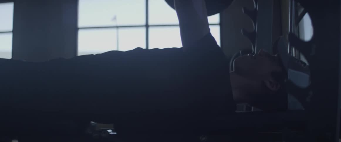 A man is benching weights in the gym during the day