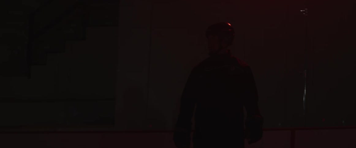 Man watches another man skate on an ice rink