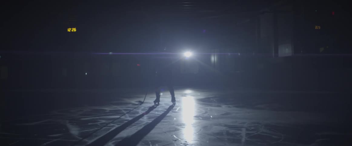 A hockey player skates on the ice in the dark