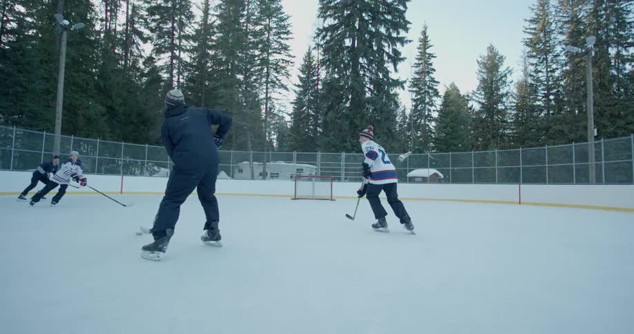 Young men play hockey on a rink outside during the day