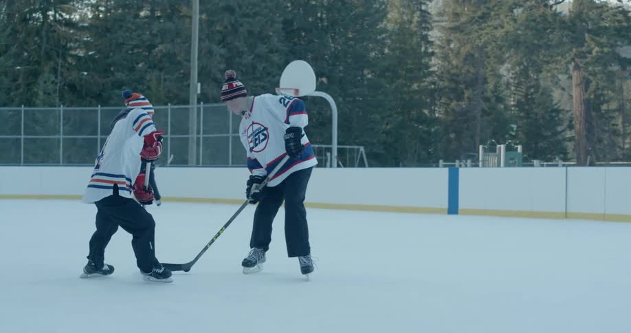 Two men play hockey on an outdoor rink