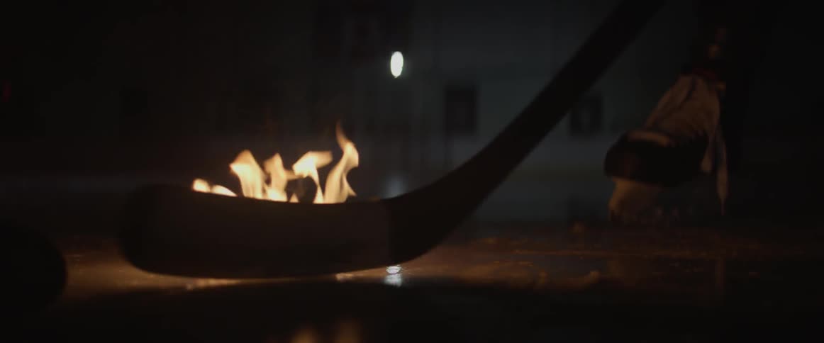 A flaming puck is dropped on the ice for face off in a dark rink