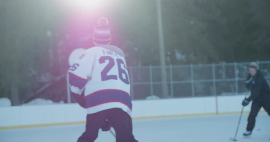 Two people wearing toques practice hockey on an outside rink