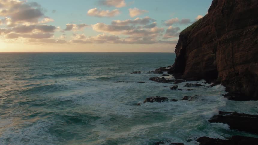 Waves crash over rocks at the base of cliffs