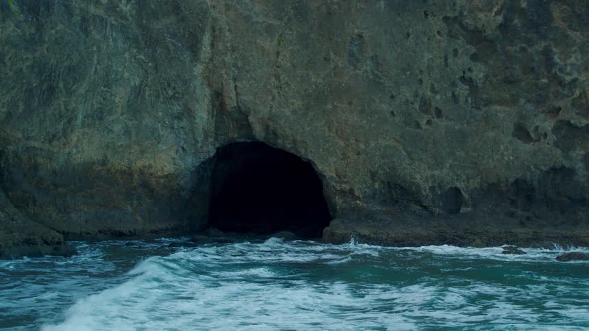 Waves lap the entrance of a cave at the base of a cliff