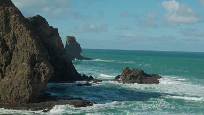 Waves crash over rocks at the base of cliffs
