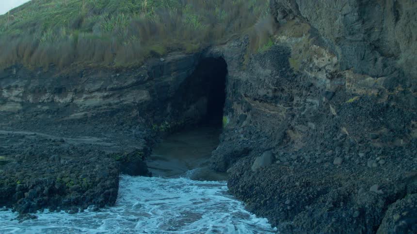 Ocean water flows back out of a cave as waves splash against the rocks