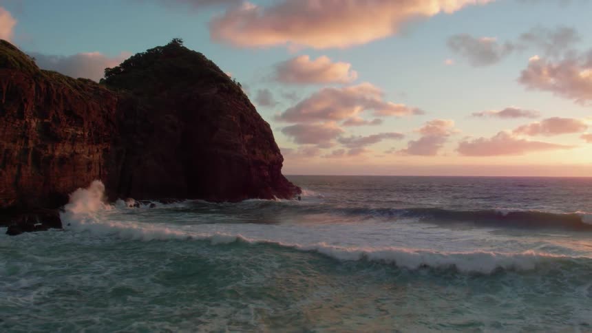 Waves crash against a large rocky hill
