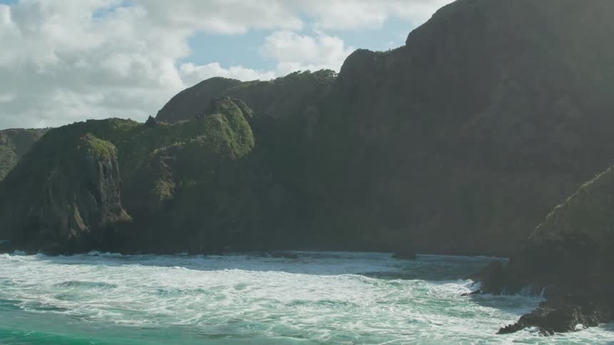 Waves crash over rocks and at the base of cliffs