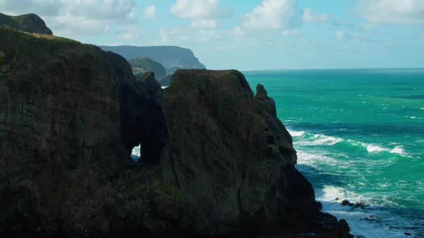 Waves crash over rocks and at the base of cliffs