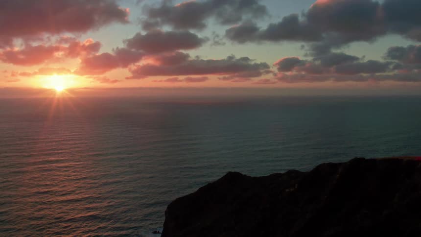 The sun is setting beyond cliffs on the coast
