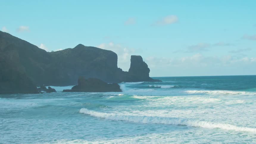 Waves crash over rocks at the base of cliffs as they roll toward the beach