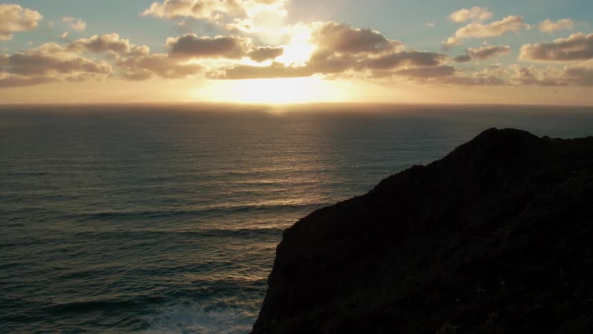 The sun sets on the horizon as waves break on the rocks