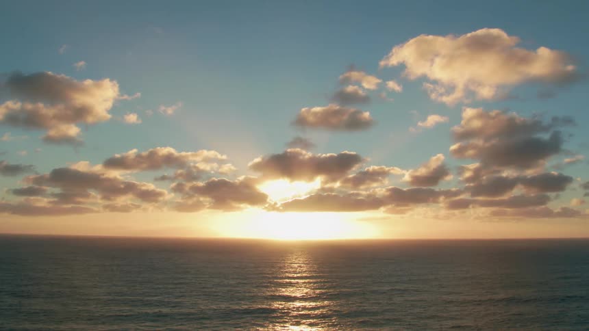 The sun is setting in a cloudy sky on an ocean horizon