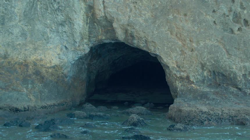 Water trickles into the mouth of a cave on a beach