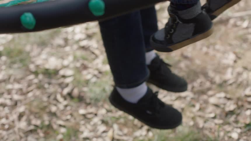 A man is pushing two children in a swing during the day