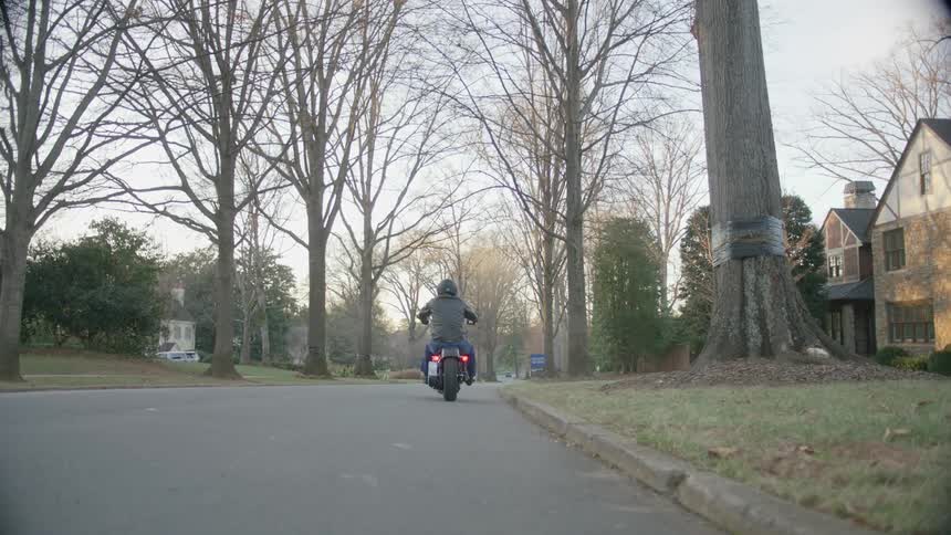 A man starts his bike kicks up the stand and rides down the neighborhood road
