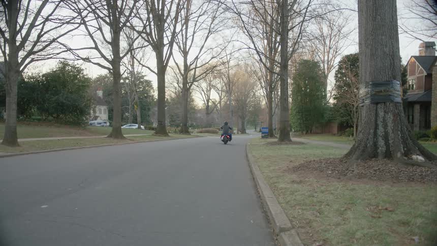 A man starts his motorcycle and rides off down a suburban street
