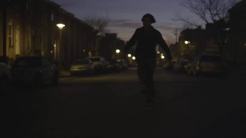A man skateboards down a city street at dusk