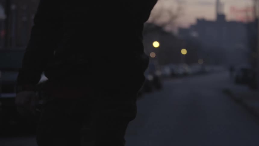 A man skateboards down a city neighborhood street with cars parked at sunset