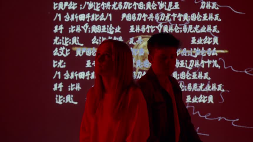 A man and woman sit in front of flashing words and pictures