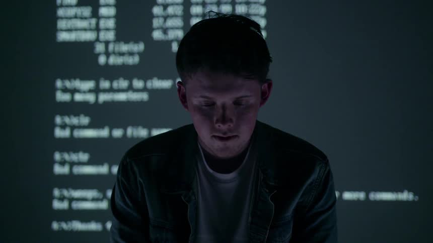 Computer text is projected on a screen behind a young man