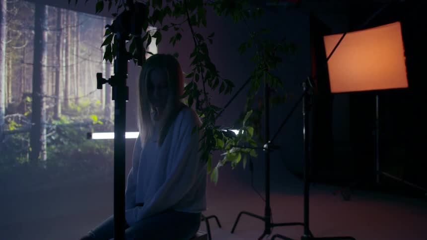 A young woman is sitting in a studio with plants and an image
