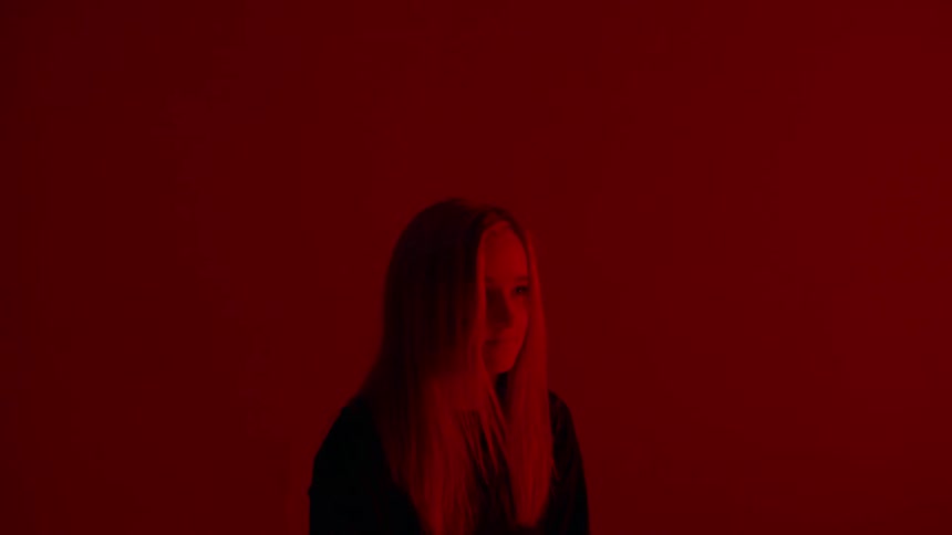 Woman stands in front of red wall with flashing lights