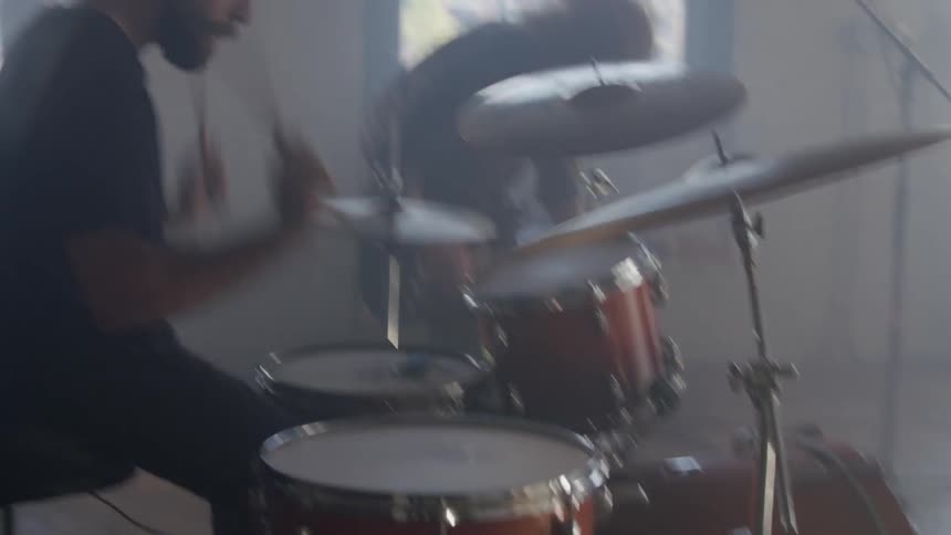 A man plays the drums while another plays a guitar in a rock band