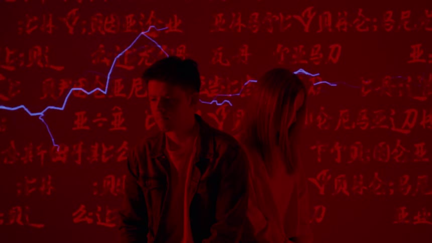 Man and woman sit in a red room with words flashing on the wall