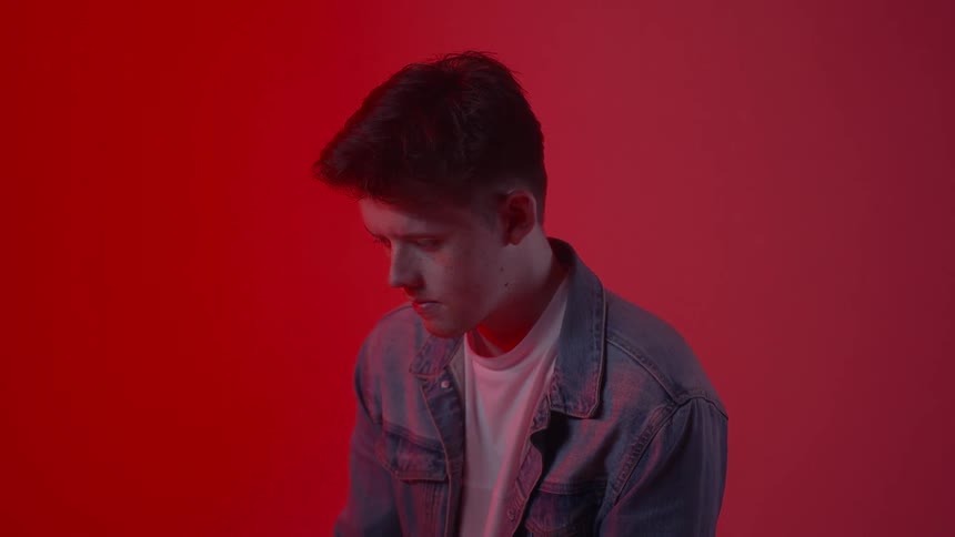 A man in a jean jacket sits in a red room
