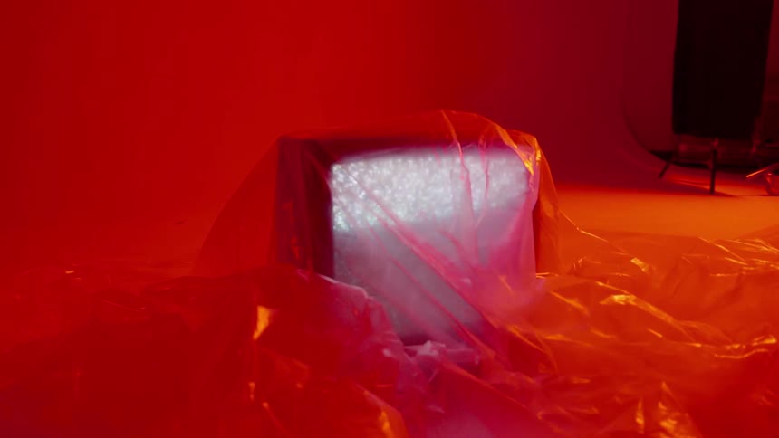 A television sitting on the floor and covered in a plastic sheet is playing static