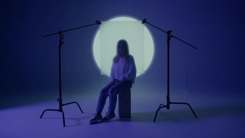 A young woman is sitting partly covered by an opaque circle in a studio