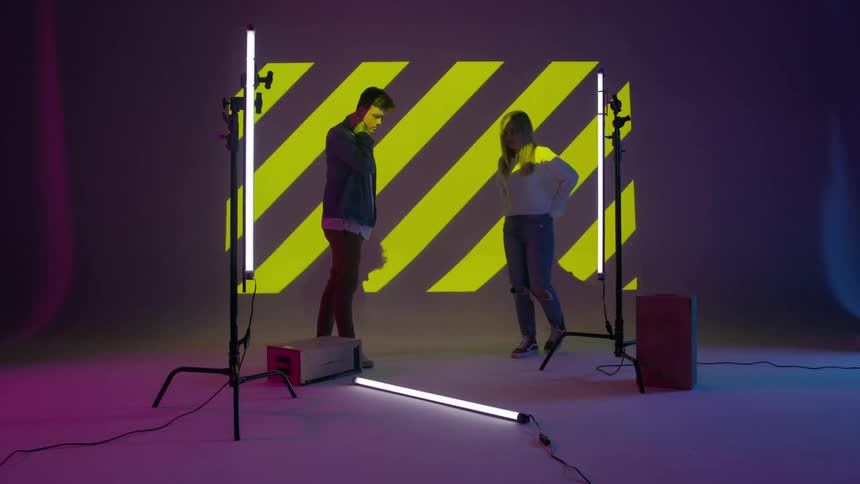 A young man and woman mill about in a room with lights and a projection