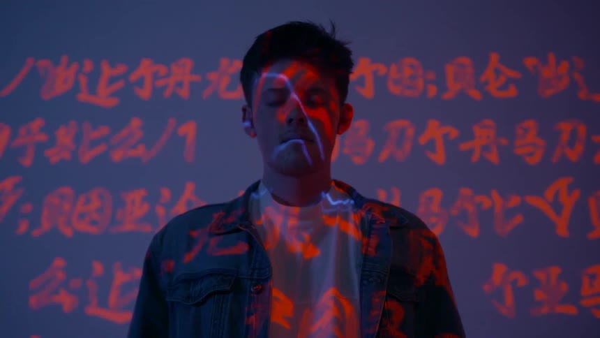 Chinese characters and lightning project on a wall behind a young man