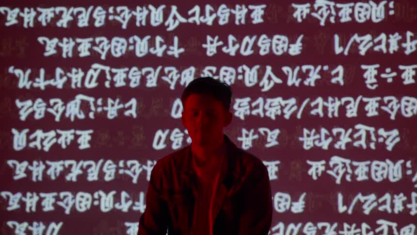 Man stands in front of a wall that is flashing chinese characters