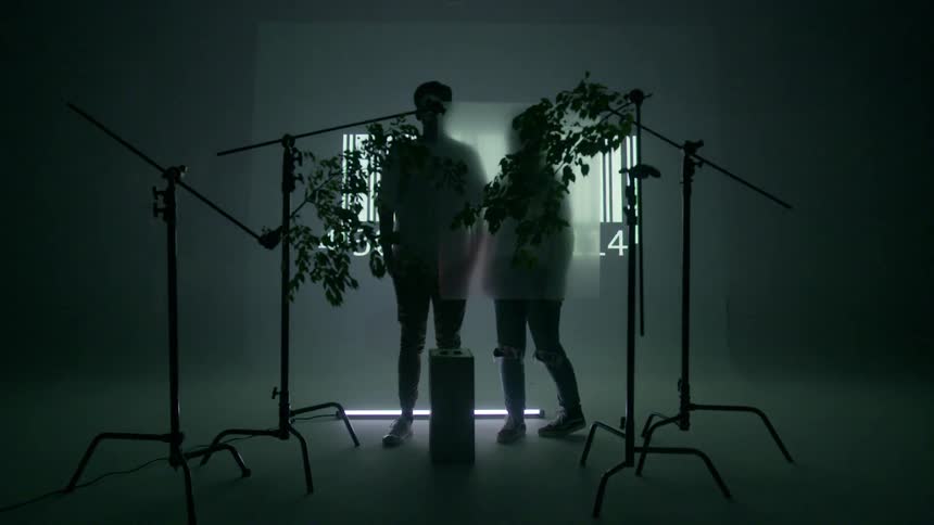 A woman walks towards a man in a room with a barcode flashing on a screen