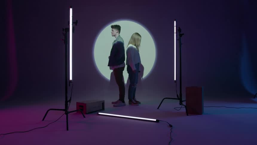 A young man and woman stand in a studio with a light projected behind them
