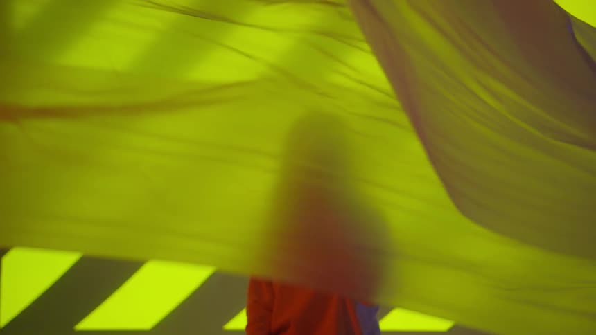 A young woman stands behind a waving yellow cloth