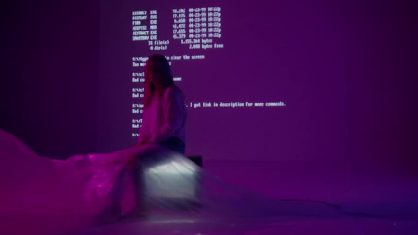A woman is sitting on a television in front of a wall projecting text