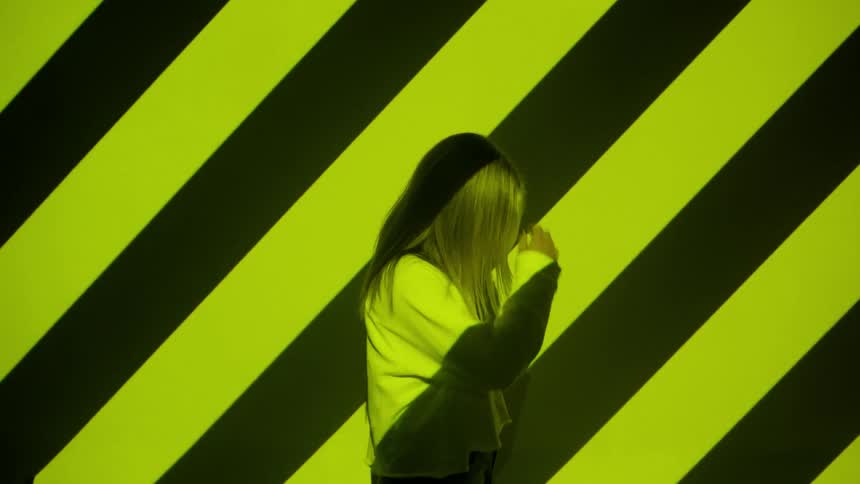 A woman is turning as she stand in front of a wall with stripes
