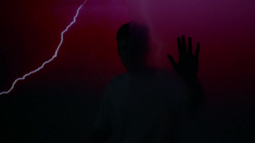 A man has his hands on an opaque board as lightning and color flash around him