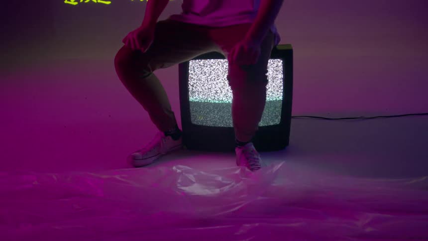 A man is sitting on a television in front of a wall of projected text