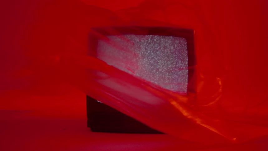 A tv plays static in a red room while a red sheet billows around it