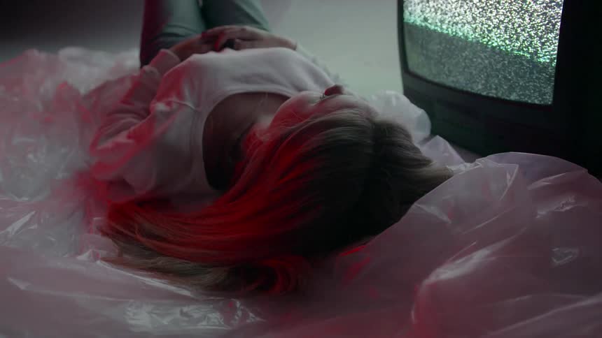A woman is laying on plastic sheets on the ground next to a television