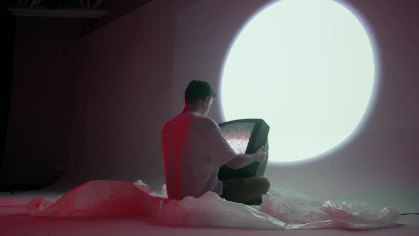 A man is sitting on plastic sheeting on the floor holding a television
